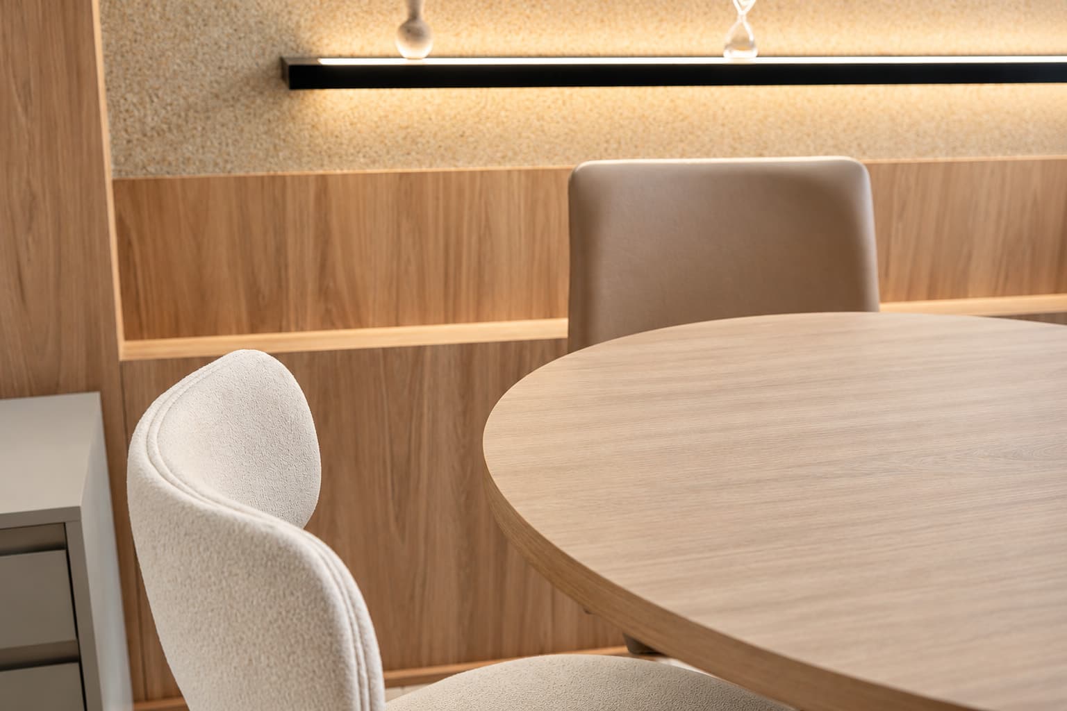 Sala de reunião com mesa em madeira, cadeiras estofadas e painel ripado com prateleira iluminada